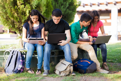 Group of teenagers social networking using several tech devices in high school