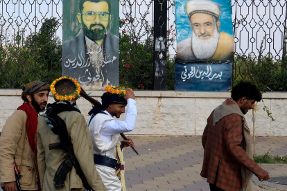 Personas armadas pasan junto a pinturas que representan a líderes hutíes fallecidos, expuestas en una valla en Saná, Yemen, el 7 de septiembre de 2026.