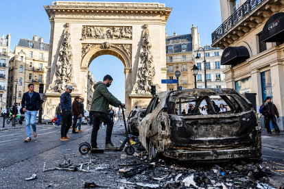 La gente pasa junto a un coche calcinado tras los enfrentamientos entre la policía antidisturbios y los manifestantes en París.
