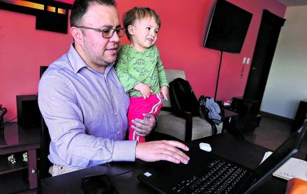 Carlos Maya, en su vivienda, cargando a su hijo mientras revisa correos.