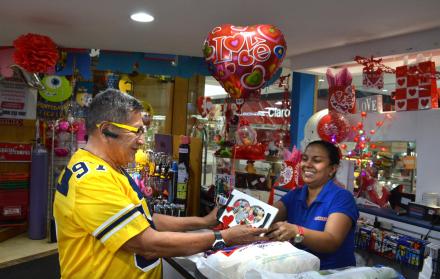 Actividad. Una sonriente vendedora muestra a un hombre una opción de regalo por San Valentín.