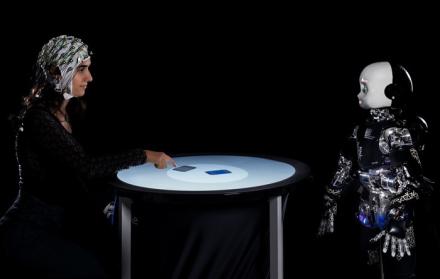 Una persona y un robot humanoide participan en un juego competitivo, mientras se mide su actividad cerebral con un electroencefalograma.