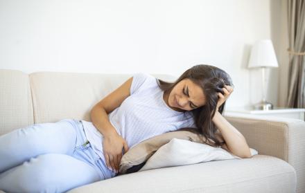 woman-in-painful-expression-holding-hands-against-belly-suffering-menstrual-period-painsitting-sad-on-home-bed-having-tummy-cramp-in-female-health-concept