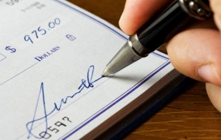 Primer plano de una mano que firma un cheque.