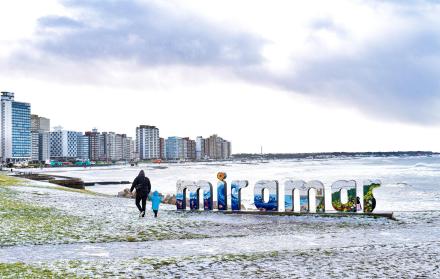 Personas caminan en una playa cubierta de nieve este lunes 30 de junio de 2025, en Miramar (Argentina).