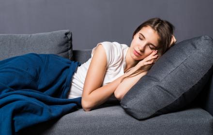 nina-durmiendo-en-un-sofa-cubierto-con-colcha-azul-sobre-fondo-gris