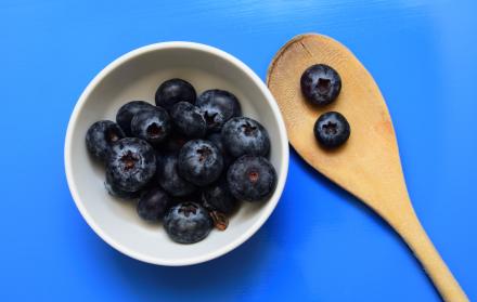 disparo-de-alto-angulo-de-un-recipiente-blanco-con-arandanos-cerca-de-una-cuchara-de-madera-aislada-en-una-pared-azul