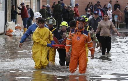 Integrantes de organismos de rescate socorren a un hombre en una calle inundada
