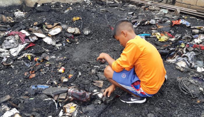 El pequeño Daniel (nombre protegido) busca entre los escombros quemados algún implemento que sirva para levantar el lugar.