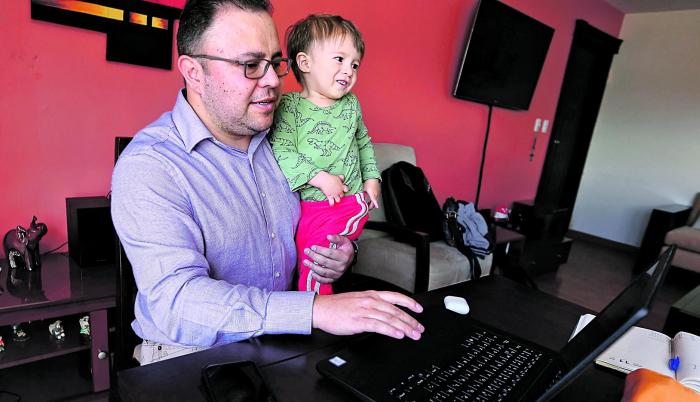 Carlos Maya, en su vivienda, cargando a su hijo mientras revisa correos.