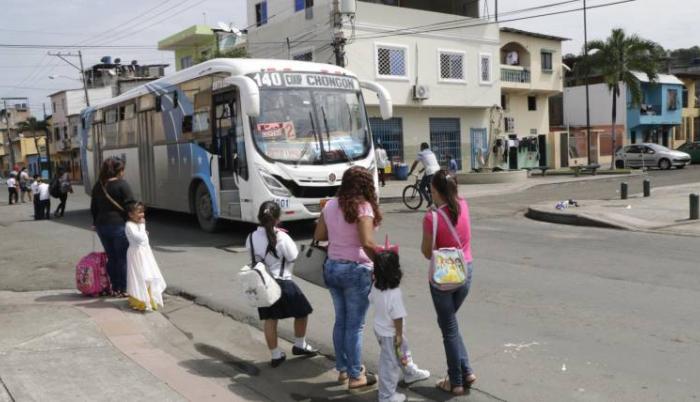 Varios padres de familia y sus hijos esperan la ausencia de vehículos en la avenida 10 de agosto en el barrio Garay para cruzar la calle.