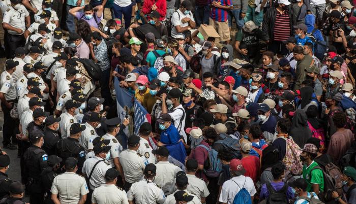 Migrantes hondureños se arrodillan para orar frente a los policías guatemaltecos, el 17 de enero de 2021 desde la aldea Vado Hondo, Chiquimula (Guatemala).