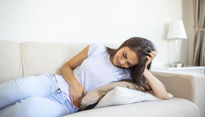 woman-in-painful-expression-holding-hands-against-belly-suffering-menstrual-period-painsitting-sad-on-home-bed-having-tummy-cramp-in-female-health-concept