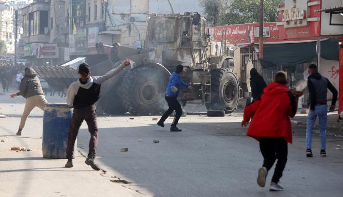 Palestinos lanzan piedras en medio de enfrentamientos con tropas israelíes durante una incursión en Yenín, Cisjordania, este 26 de enero.