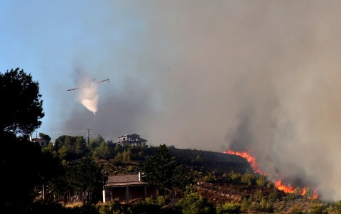 Un avión de extinción de incendios arroja agua durante un incendio forestal que estalló en una zona de tierras de cultivo y bosques en Varnavas, región de Ática, Grecia.