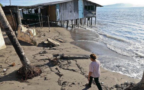 Una mujer caminando frente a una vivienda afectada en la costa de la comunidad de Cedeño (Honduras).