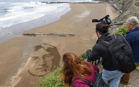 El artista peruano Germán Cedano trabaja en una playa del norte de España, donde graba en la arena la imagen del músico John Lennon.