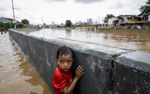 YAKARTA. Un niño se protege tras un muro en una carretera inundada.