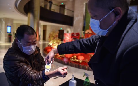WUHAN. El administrador de un hotel toma la temperatura de un viajero que pide hospedaje.
