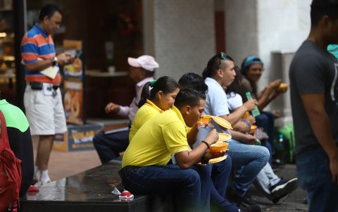 Trabajadores y transeúntes del centro de la ciudad se sienta en bancas a comer.