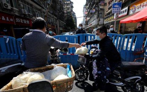 WUHAN. Un hombre entrega comida a los residentes de un barrio que quedó detrás de una barrera durante la cuarentena.