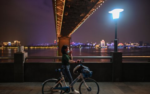WUHAN, CHINA: Una mujer con una máscara facial camina junto a su bicicleta en una plaza a lo largo del río Yangtze en el epicentro de la pandemia.