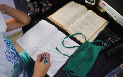 Un niño escribe en su cuaderno mientras mira una clase en la televisión en su casa en La Habana