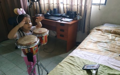 Valentina Torres toca los bongós mientras recibe la clase a través de una plataforma digital.