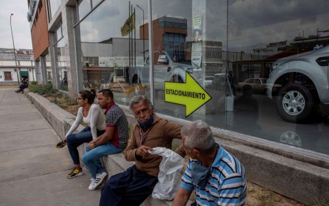 Espera. Personas descansan este jueves en una acera mientras esperan junto a sus vehículos para comprar gasolina en una estación de servicio.