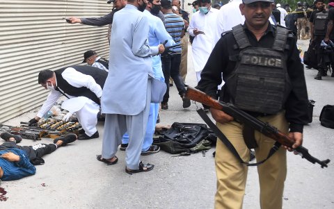 KARACHI. Personal de seguridad inspecciona las armas recuperadas junto al cuerpo de un presunto pistolero frente al edificio de la Bolsa de Valores de Pakistán.
