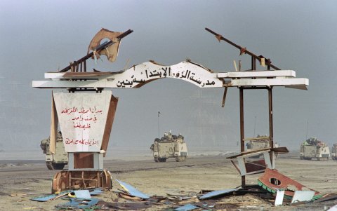 AL-AHMADI. Vehículos blindados ligeros sauditas pasan cerca de un arco bombardeado de una escuela cerca de esta ciudad, mientras las fuerzas aliadas continúan avanzando.