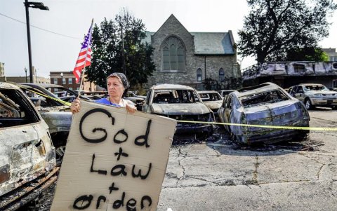 Una mujer sostiene una bandera estadounidense y un letrero que lee 