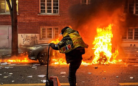 Un hombre se desplaza cerca de un coche en llamas.