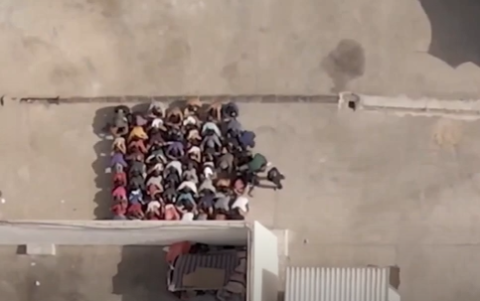 Denegado el permiso de visitar el centro de detención de Al Mabani, un dron captó una escena del patio interior con 65 migrantes arrodillados mientras los guardias golpean a uno de ellos por mirar hacia los lados.