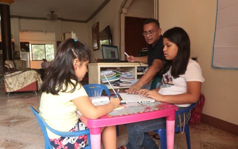 El profesor Henry Ramos revisa las tareas escolares de sus hijas mientras interactúa de modo virtual con sus alaumnos.