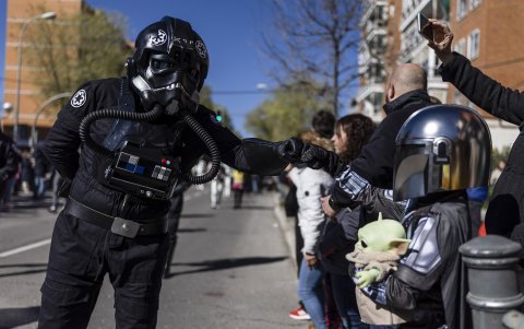 Un piloto del cuerpo imperial de cazas estelares TIE de la saga Star Wars (i) saluda a un pequeño mandaloriano (d) durante el desfile del Galaxy Day por una calle de Madrid.