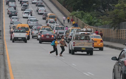 Estudiantes junto a sus padres caminan en medio de los vehículos de transitan por la vía.
