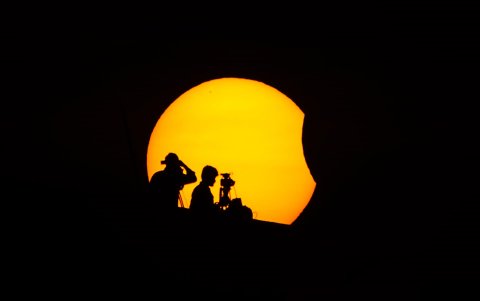 El personal de los medios se encuentra en lo alto de un edificio mientras la luna cubre parcialmente el sol durante un eclipse solar parcial, en Marina Beach, en Chennai, India.