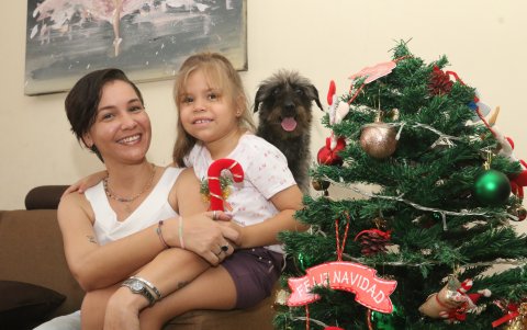 Figura. Amaya colocó el tradicional árbol navideño en la sala de su casa y posa con su hija y su perro.