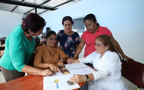La adulta mayor, vistiendo su uniforme blanco de colegio, rodeada de los maestros que le han brindado conocimientos.