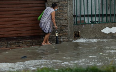 Una señora trata de caminar descalza por la vereda completamente inundada. Esto es una molestia para los peatones.