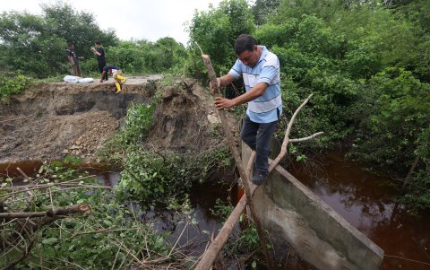 Las personas deben pasar la carretera rota con un improvisado puente hecho por ramas de árboles