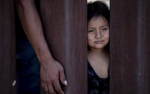 Janina (derecha), niña ecuatoriana de 4 años, mira a través del muro fronterizo mientras espera con su padre Jaime (izquierda) que los agentes de la Patrulla Fronteriza la lleven a un centro de procesamiento a lo largo de la frontera entre México y Estados Unidos.