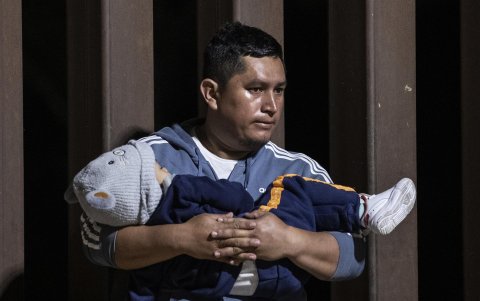 Un padre migrante sostiene a su hijo en brazos mientras espera ser procesado por agentes de la Patrulla Fronteriza después de cruzar ilegalmente la frontera entre Estados Unidos y México.