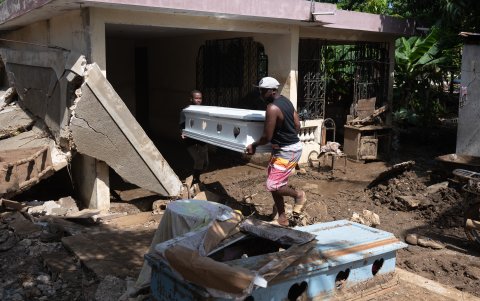 Dos hombres cargan un cajón junto a una vivienda dañada en una calle llena de lodo producto de las intensas lluvias, hoy, en Leogane (Haití).