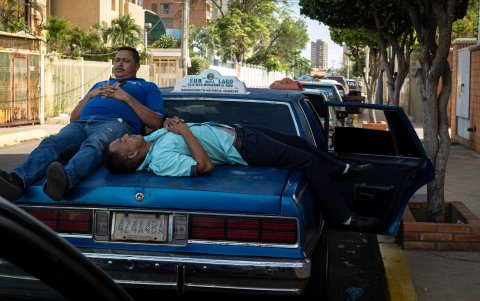 Dos hombres descansan mientras hacen fila junto a sus vehículos para surtir combustible el 13 de junio de 2023, en Maracaibo (Venezuela).