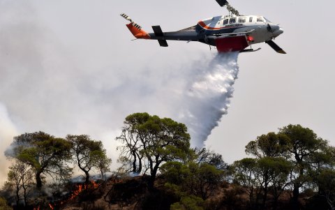Un avión de extinción de incendios arroja agua para extinguir un incendio forestal que está quemando una zona forestal frente a las instalaciones de la refinería de Motor Oil,  Grecia.