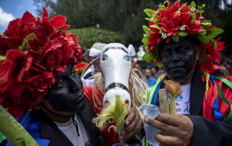 Los participantes llevan sacos negros, pantalones blancos y gorros de flores.