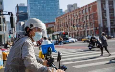 Un hombre con una máscara facial monta un scooter en una calle de Beijing, China, el 21 de agosto de 2023.