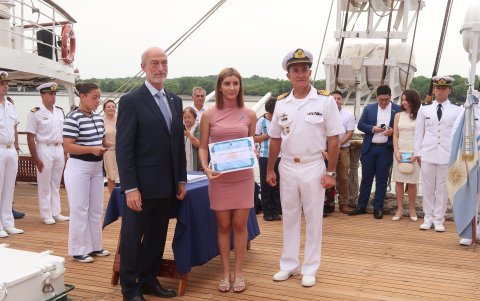 El embajador Eduardo Acevedo Díaz entrega un certificado por el Acto de Promesa a la Bandera Nacional a Natali Spina Graziano. Los acompaña el capitán de navío Gonzalo Nieto.